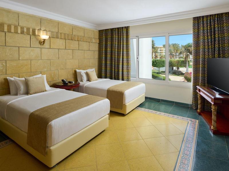 Hotelový pokoj s dvěma jednolůžky, televizí a skleněnými dveřmi vedoucími ven.