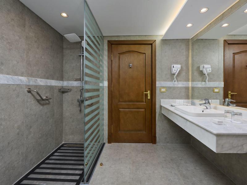 Moderní hotelová koupelna se dřevěnými dveřmi, skleněnou přepážkou sprchy a dvojitým umyvadlem.