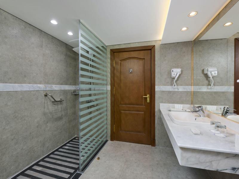 Moderní hotelová koupelna se sprchovým koutem bez vaničky, dřevěnými dveřmi a mramorovou umyvadlovou deskou.