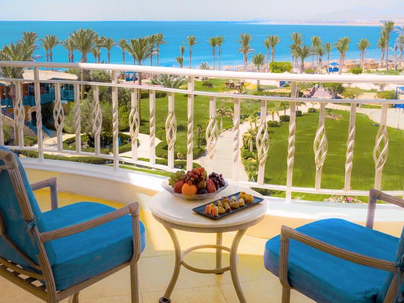 Balkon s modrými židlemi a stolem s výhledem na palmy a oceán.