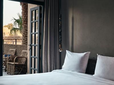 Habitación de hotel con ventana abierta, almohadas blancas y vista a terraza con muebles de ratán.