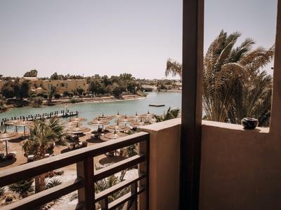 Vista desde un balcón hacia un río con barcos y una playa soleada del hotel con tumbonas y sombrillas.