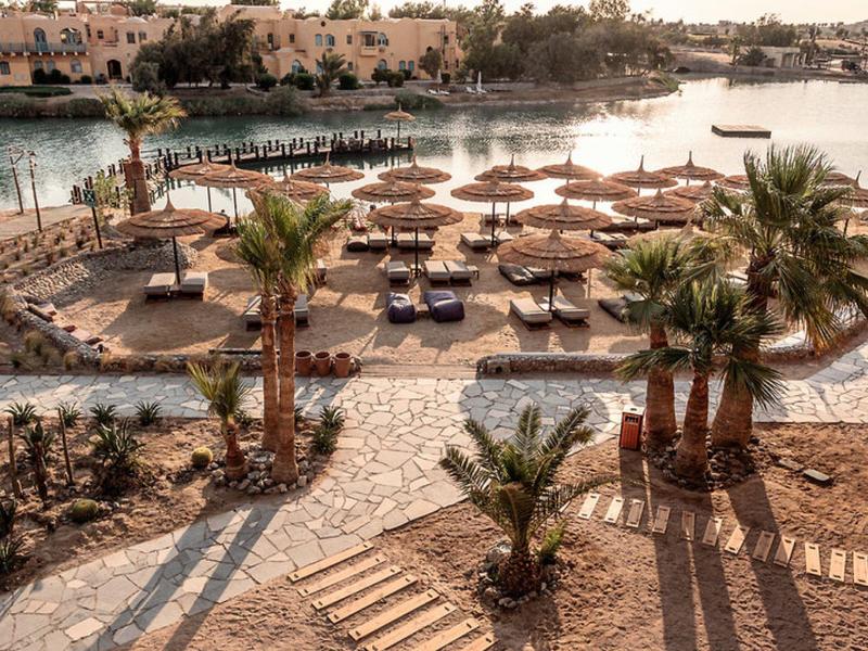 Strand mit Sonnenschirmen, Palm Bäumen und ruhigem Wasser im Hintergrund bei Sonnenuntergang.