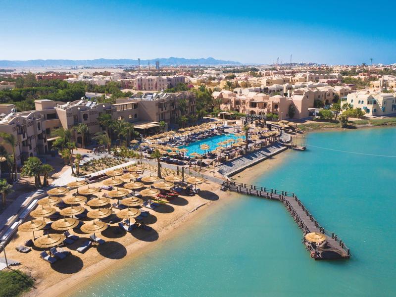 Strand mit Strohm Sonnenschirmen, Holzsteg und blauem Meer an sonnigem Himmel.
