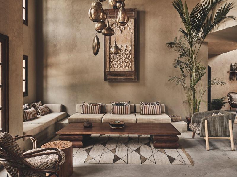 Modernes Wohnzimmer in warmen Erdtönen mit Holzmöbeln, Teppich, großen Fenstern und Palmenpflanze.