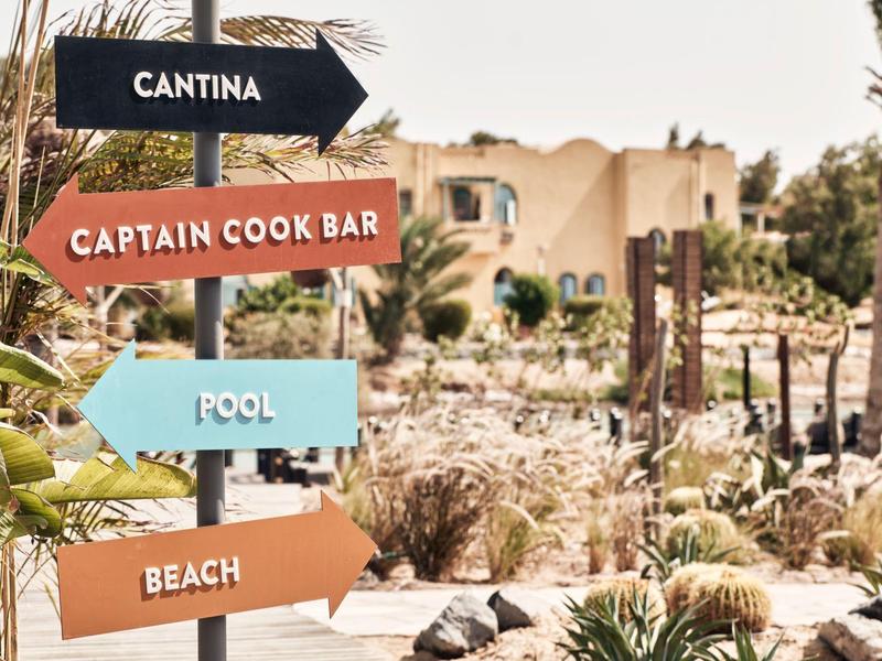 Bunte Wegweiser aus Holz zeigen Richtungen zu Cantina, Captain Cook Bar, Pool und Strand.