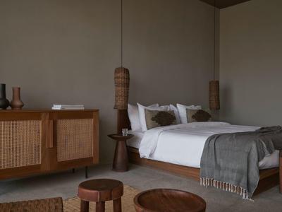 Schlichte Schlafzimmer mit Holzmöbeln, weißer Bettwäsche und grauer Decke, gedeckte Naturfarben.