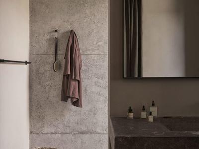 Modernes Badezimmer mit grauen Steinwänden, großem Spiegel, Handtüchern und geflochtenem Korb.