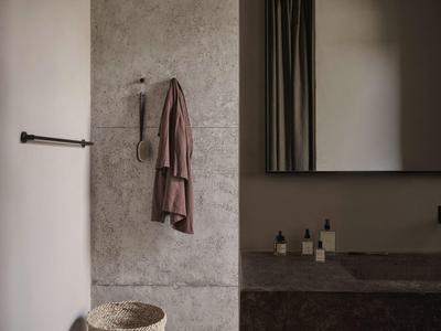 Modernes Badezimmer mit grauen Fliesen, braunem Handtuch und Waschtisch mit Spiegel.