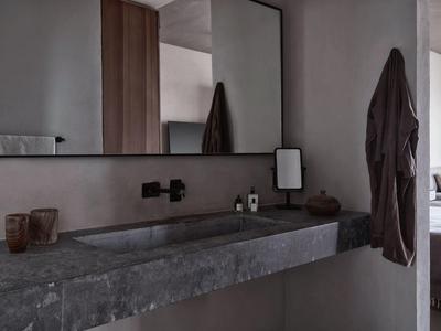 Moderner Badezimmerbereich mit großem grauem Steinwaschbecken, Wandspiegel und dunklem Handtuch.