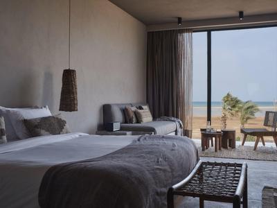 Modernes Schlafzimmer mit großem Bett, Sofa, Sessel und bodentiefem Fenster mit Meerblick.