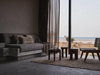 Modernes Wohnzimmer mit grauem Sofa, Holzmöbeln, Teppich und großem Fenster mit Meeresblick.