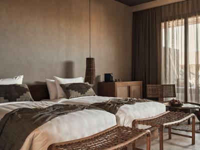 Modern hotel room with two single beds, wooden furniture, and daylight from large windows.