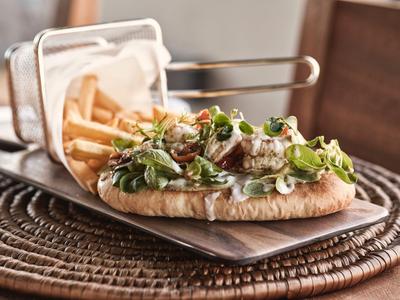 Frisches Sandwich mit Salat, Tomate und Oliven, serviert auf Holztablett mit Pommes Frites.