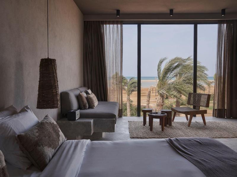 Hotelzimmer mit Fensterfront, Meerblick, Sofa, Bett und modernem Holzdesign.