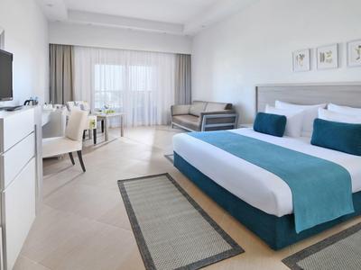 Helles, modernes Schlafzimmer mit großem Bett, TV, Schreibtisch und Balkonfenstern.