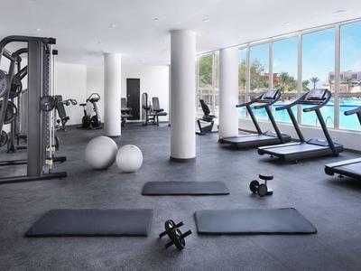 Moderne Fitnessraum mit Laufbändern, Gewichten, Matten und großen Fenstern mit Poolblick.