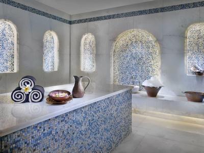 Innenraum mit verzierten blauen Mosaikfliesen, dekorativen Krügen und beleuchteten Nischen.