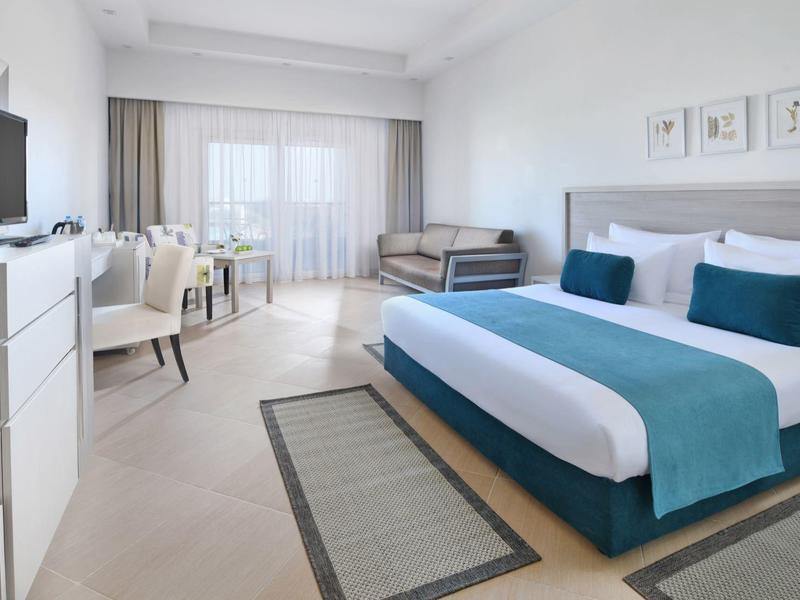 Modern ausgestattetes Hotelzimmer mit großem Bett, TV, Schreibtisch und Balkonzugang.