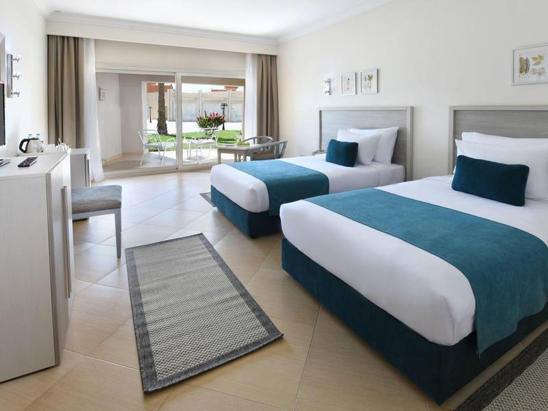 Modernes Hotelzimmer mit zwei Einzelbetten und Zugang zu einer Terrasse mit Gartenblick.