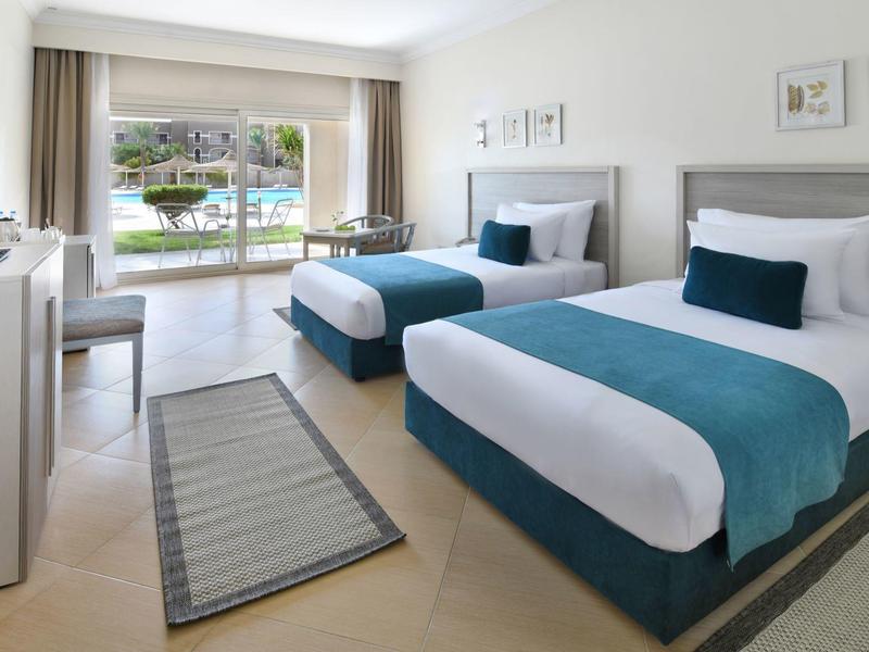 Helles Hotelzimmer mit zwei Einzelbetten, Schreibtisch und Blick auf den Balkon.