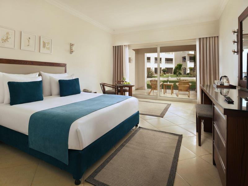 Helles Hotelzimmer mit Doppelbett, Fernseher und Zugang zu einer Terrasse mit Gartenblick.