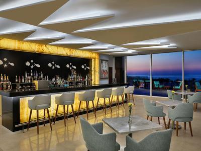 Modern hotel bar area with stylish seating and panoramic sunset view.