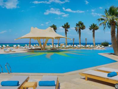 Groot hotelzwembad met ligstoelen en palmbomen onder blauwe lucht bij de zee