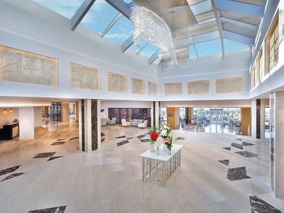 Großer heller Raum mit Glasdecke, weißen Wänden, Säulen und Blumenarrangement auf Tisch.