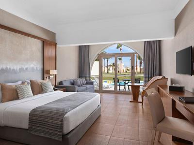 Modern eingerichtetes Hotelzimmer mit großem Bett, Schreibtisch, Flachbildschirm und Blick auf Garten.