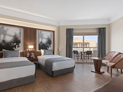 Modernes Hotelzimmer mit zwei Einzelbetten, Holzfußboden und Balkon mit Terrasse und Stühlen.