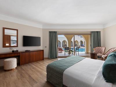Helles Hotelzimmer mit Doppelbett, Holzfußboden, Fernsehschrank und Balkon mit Meerblick.