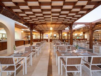 Weitläufiger Restaurantbereich mit weißen Tischen, Holzdecke und warmem Beleuchtungsakzent.