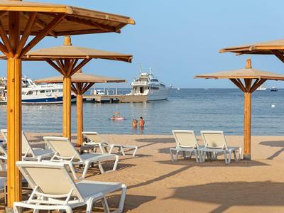 Strand mit Holzsonnenschirmen, weißen Liegestühlen und Booten im ruhigen blauen Meer.
