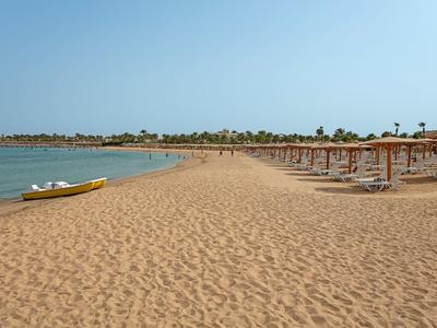 Breiter Sandstrand mit Holzsonnenschirmen und einem gelben Kajak am ruhigen blauen Meer.