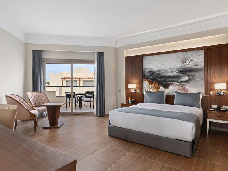 Modern hotel room with double bed, seating area, and balcony with sea view.