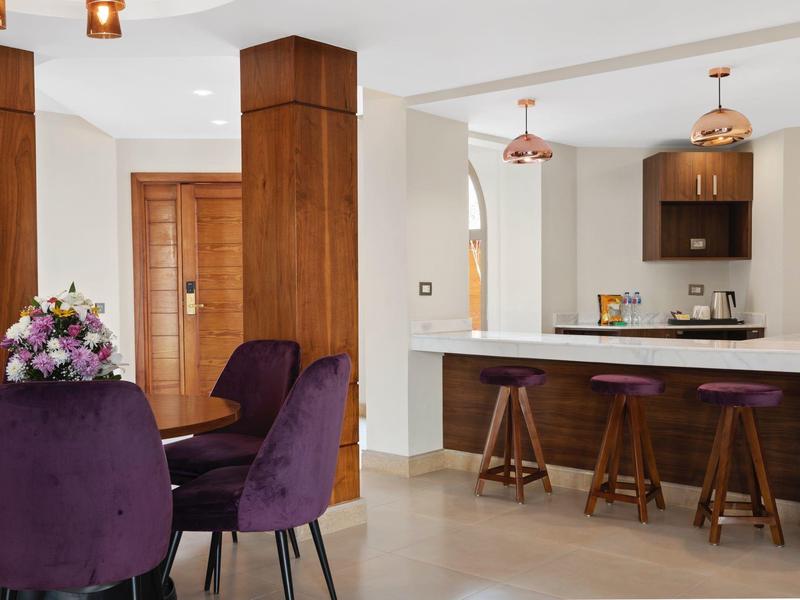 Modern dining area with purple chairs and open kitchen featuring bar stools in neutral tones.
