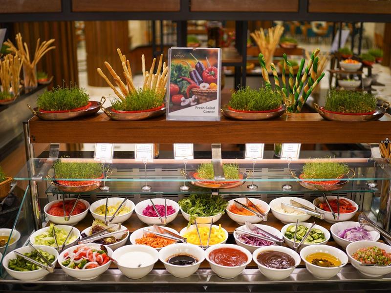 Buffet with various fresh salads and ingredients in white bowls behind glass.
