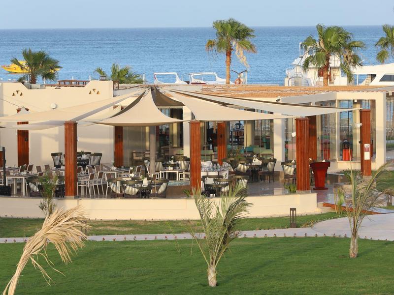 Outdoor restaurant with sunshades, green lawn, and sea view