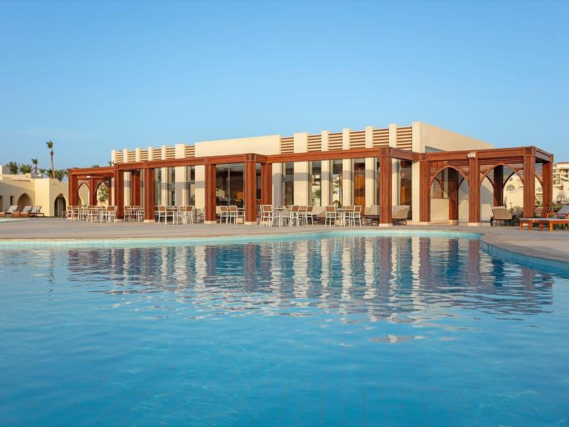 Modern building complex with large windows and columns by the clear blue pool.