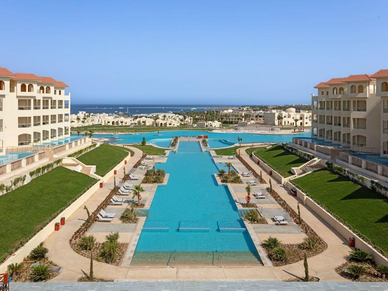 Large pool with surrounding hotels and sea view under clear sky