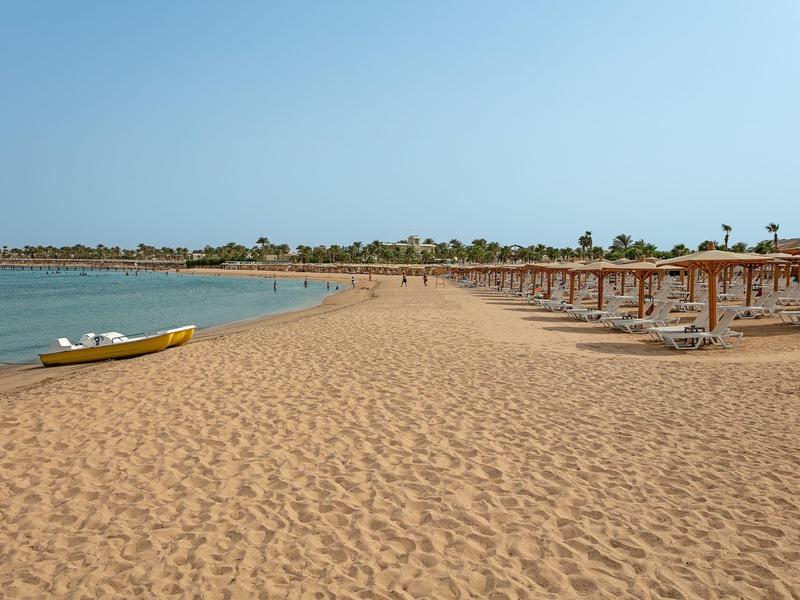 Empty sandy beach with wooden sun umbrellas and a yellow boat by calm sea