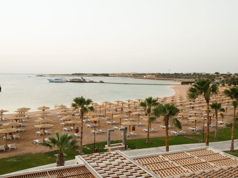 Beach with many sunbeds and umbrellas by the calm sea under an overcast sky.