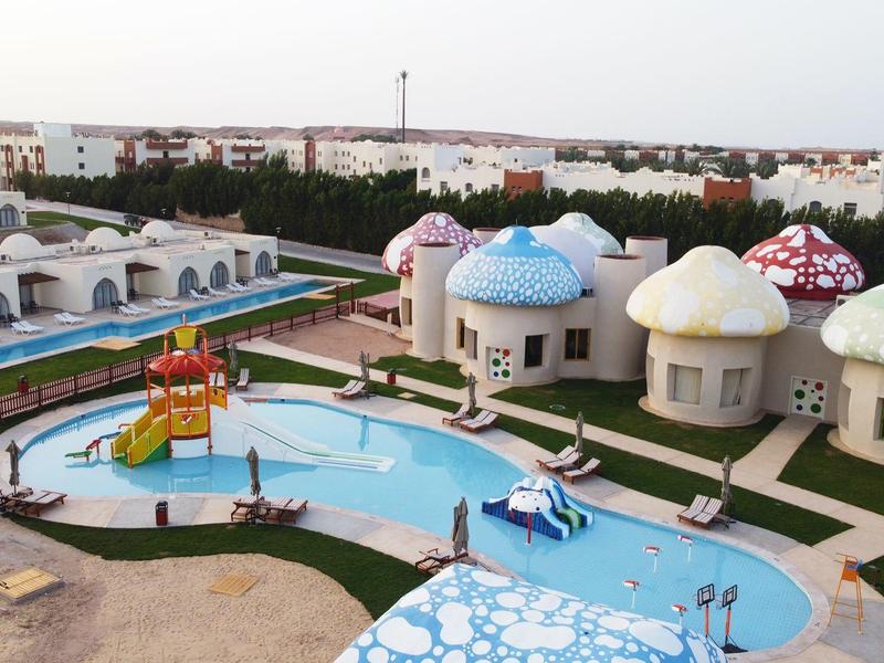 Outdoor area of a hotel with multiple small mushroom-shaped bungalows and a pool with a water slide.