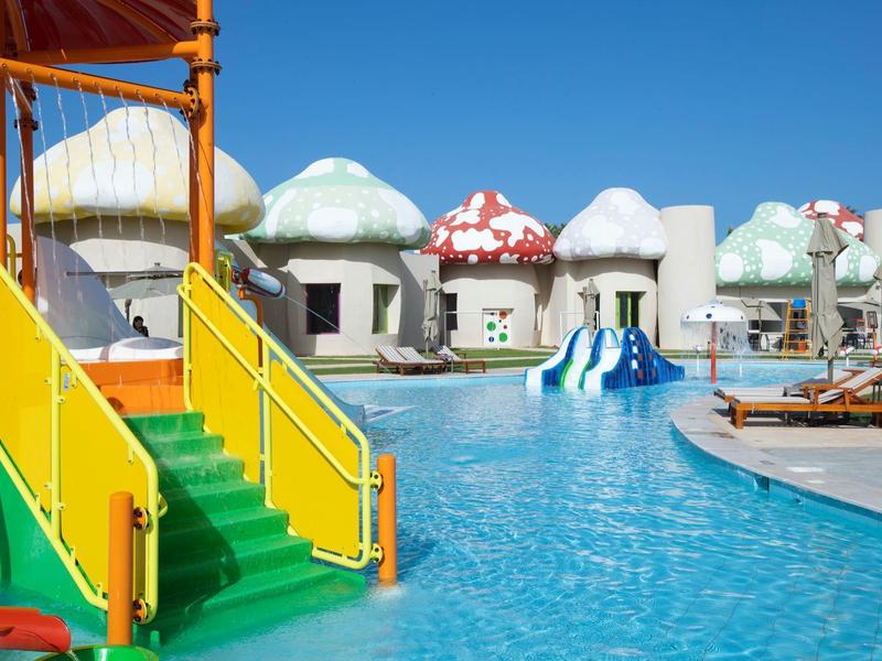 Colorful water playground with green slide and mushroom-shaped bungalows by the pool