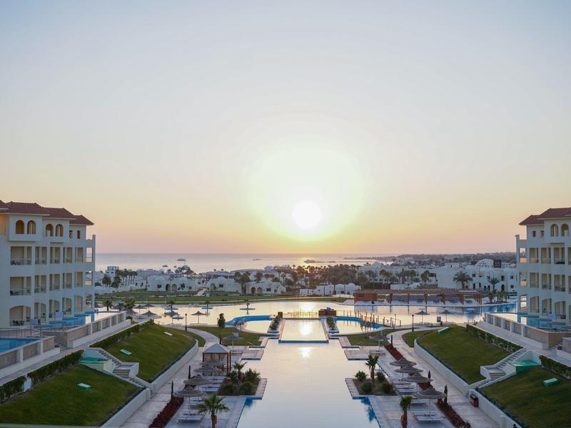 Sunset over a luxury hotel with a pool and sea view.