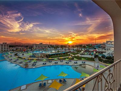 Blick von einem Balkon auf einen Hotelpool mit gelben Sonnenschirmen bei Sonnenuntergang.