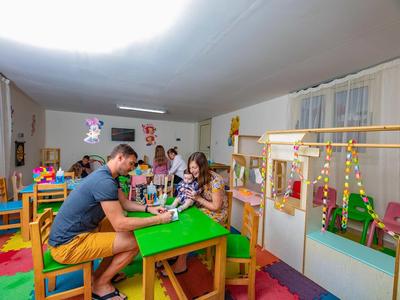 Kinder und Erwachsener spielen zusammen an einem grünen Tisch in einem bunten Spielzimmer.
