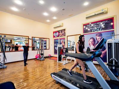 Fitnessraum mit Laufband und Trainingsgeräten in einem Hotel mit hellen Wänden und Holzfußboden.