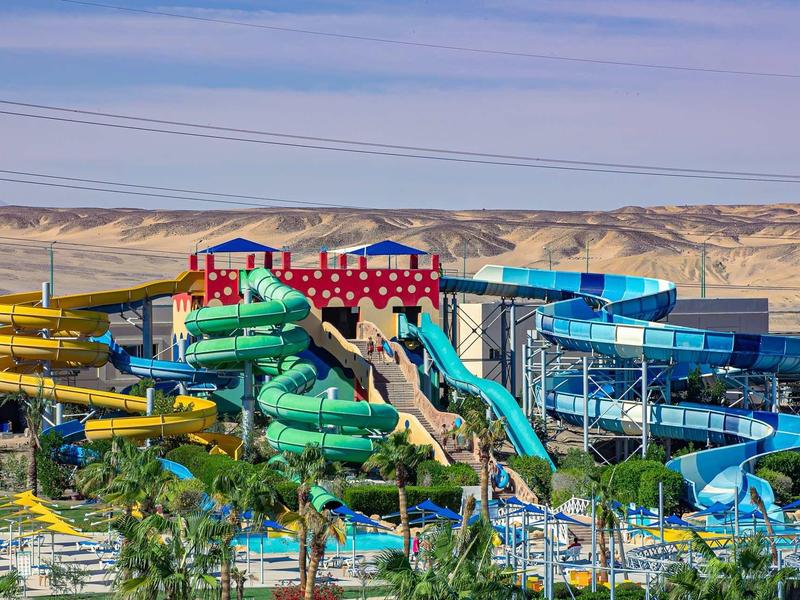 Wasserrutschen in verschiedenen Farben in einem Wasserpark vor einer Wüstenlandschaft.